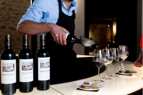 Service de vin rouge par un professionnel lors d’une dégustation élégante, illustrant l’art de recevoir dans les domaines bordelais.