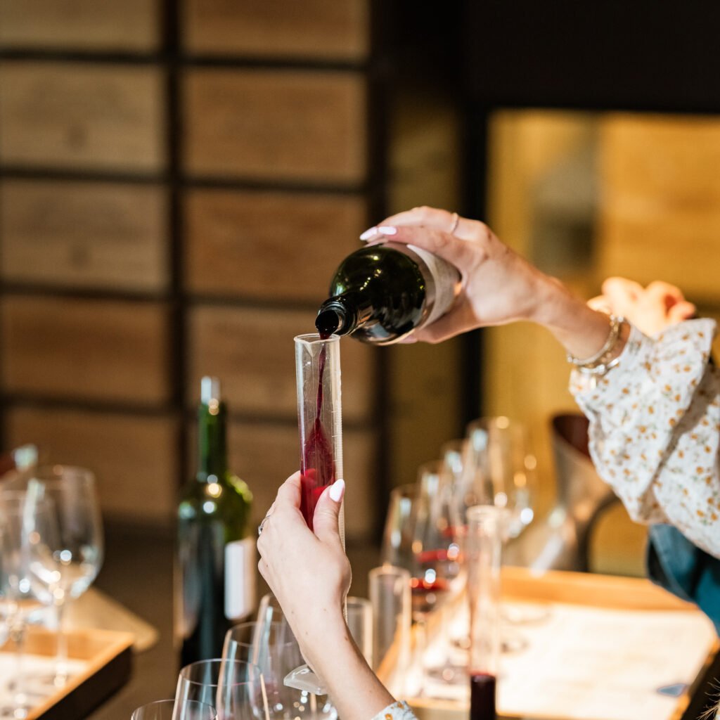 Atelier d’assemblage du vin à Bordeaux – main versant du vin rouge dans une éprouvette lors d’une dégustation œnologique.