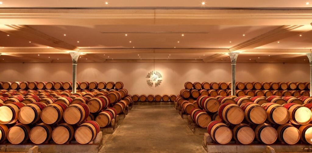 Chai de barriques dans un Grand Cru Classé de Bordeaux, offrant un cadre élégant pour une visite œnologique immersive et raffinée.