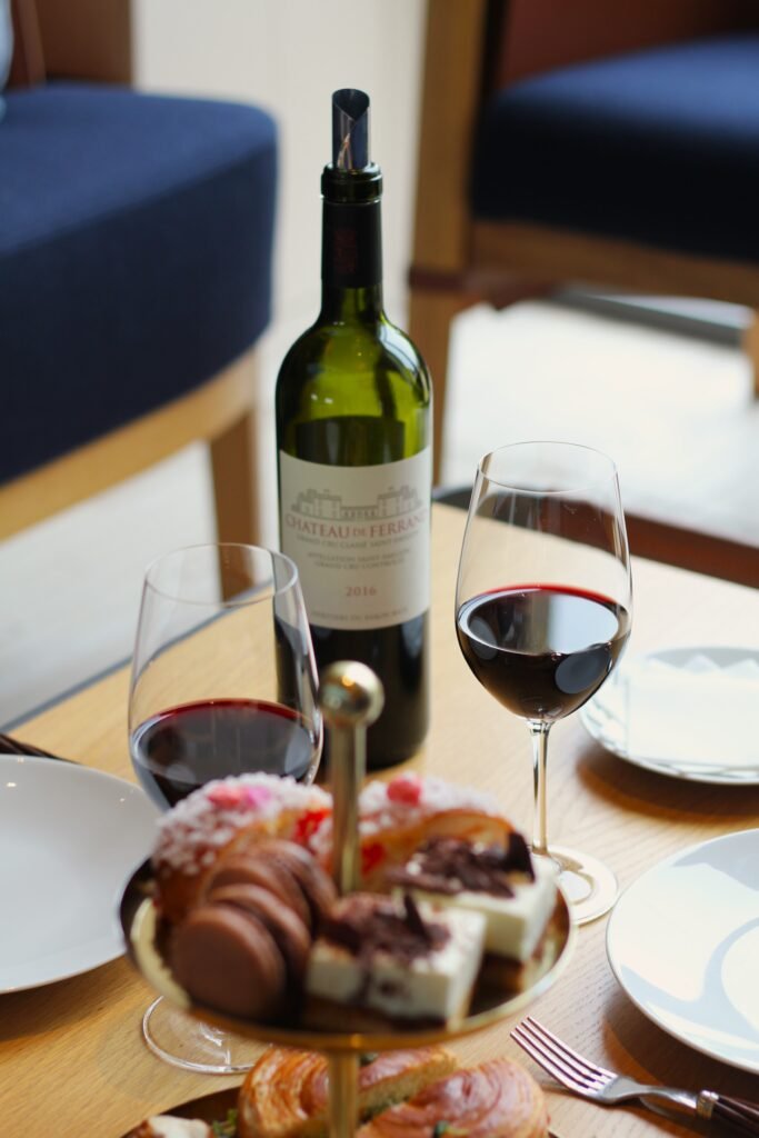 Verres de vin rouge et douceurs disposés pour une dégustation élégante, illustrant un moment raffiné dans l’univers œnologique bordelais.