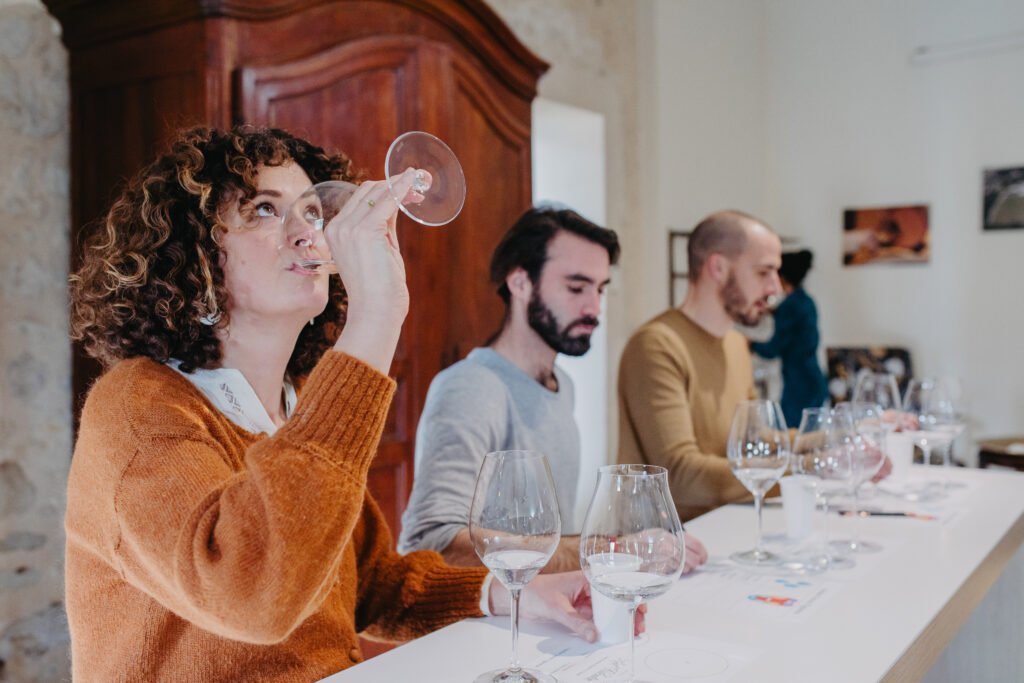 Participants assis en dégustation, levant un verre pour analyser le vin lors d’un atelier œnologique.