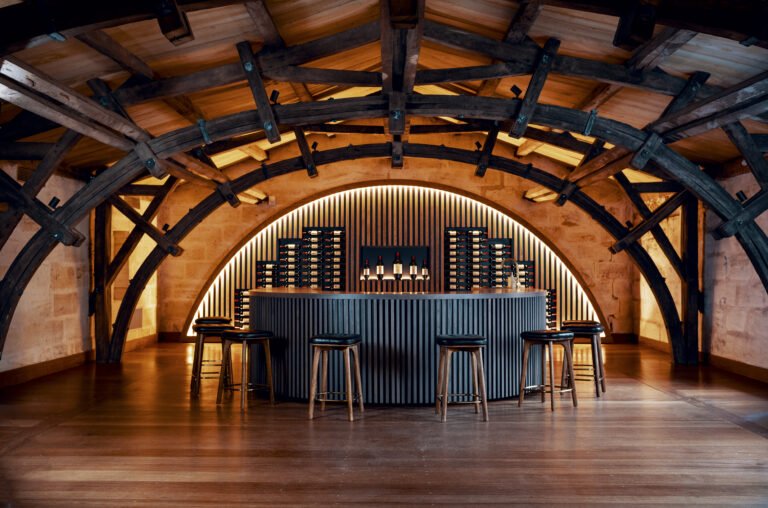 Salle de dégustation voûtée avec bar moderne et bouteilles de vin, architecture en bois au sein d’un domaine viticole à Saint-Émilion
