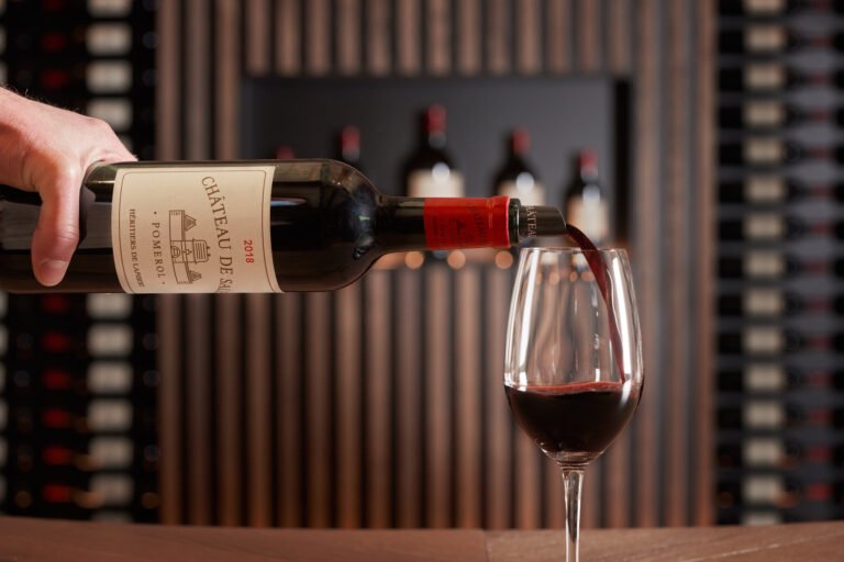 Service de vin rouge Château de Pomerol dans un verre, dégustation dans un chai moderne avec bouteilles en arrière-plan