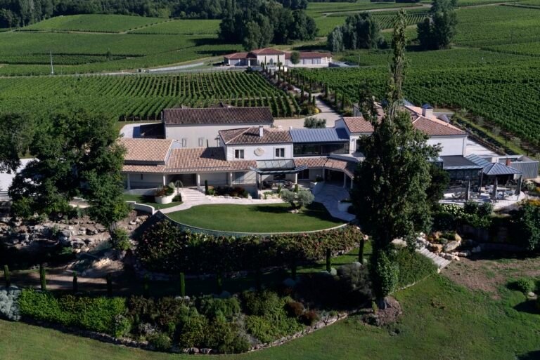 Vue aérienne d’un domaine viticole entouré de vignobles, avec bâtiments rénovés et jardins paysagers
