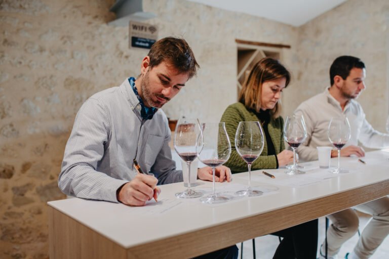 Deux participants assis notant leurs impressions devant des verres de vin lors d’une dégustation.